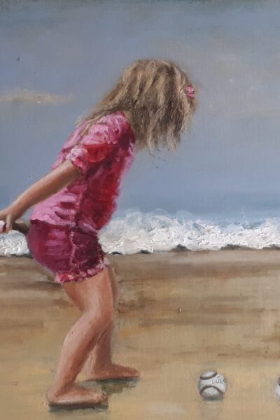 Little girl in pink practicing camogie on the beach